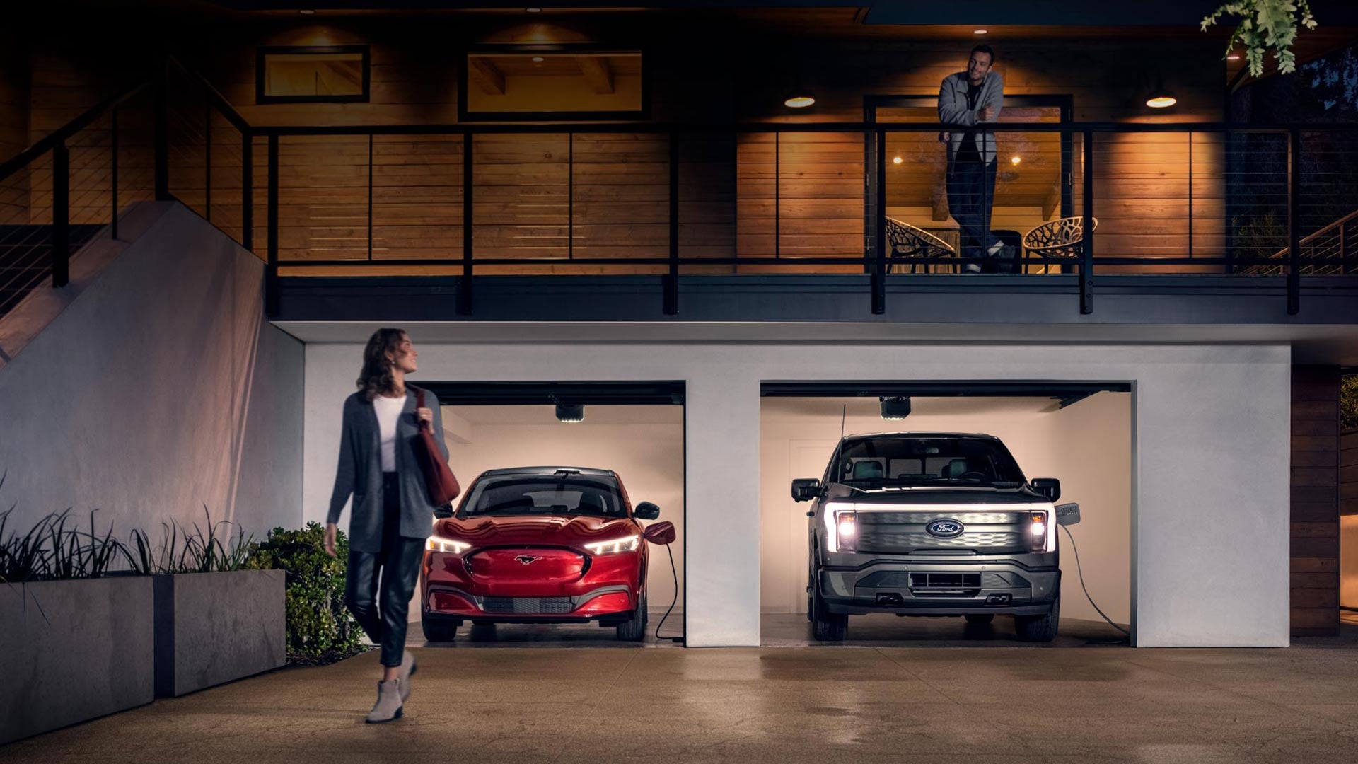 Woman walking out from home garage with a 2024 Mustang® Mach-E and Ford Lightning® truck in plugged-in and charging | Zook Motors in Kane PA